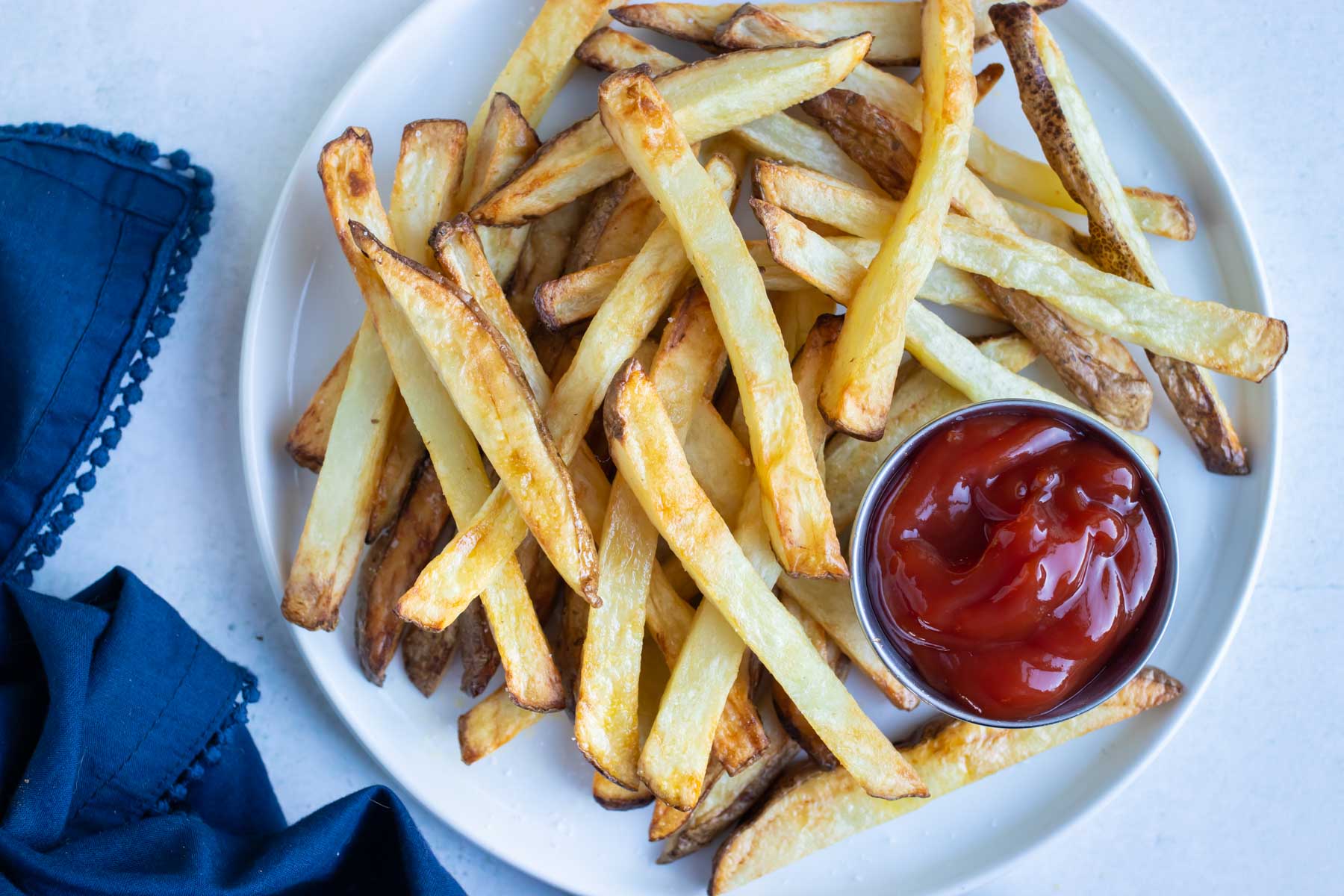 A pile of air fryer french fries are shown on a white plate on the counter.