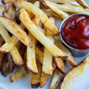 A pile of air fryer french fries are shown on a white plate on the counter.