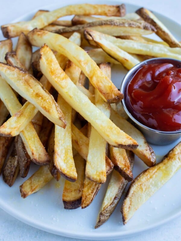 A pile of air fryer french fries are shown on a white plate on the counter.