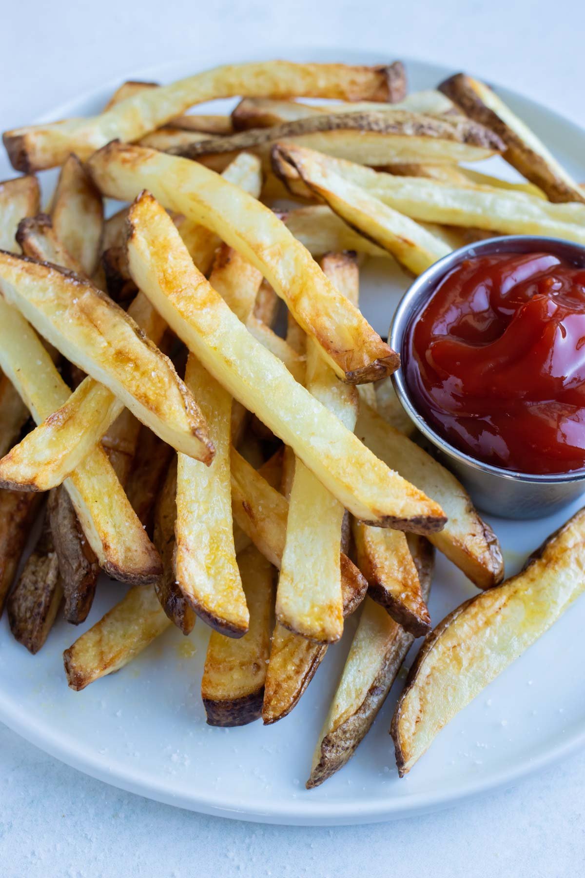 A pile of air fryer french fries are shown on a white plate on the counter.