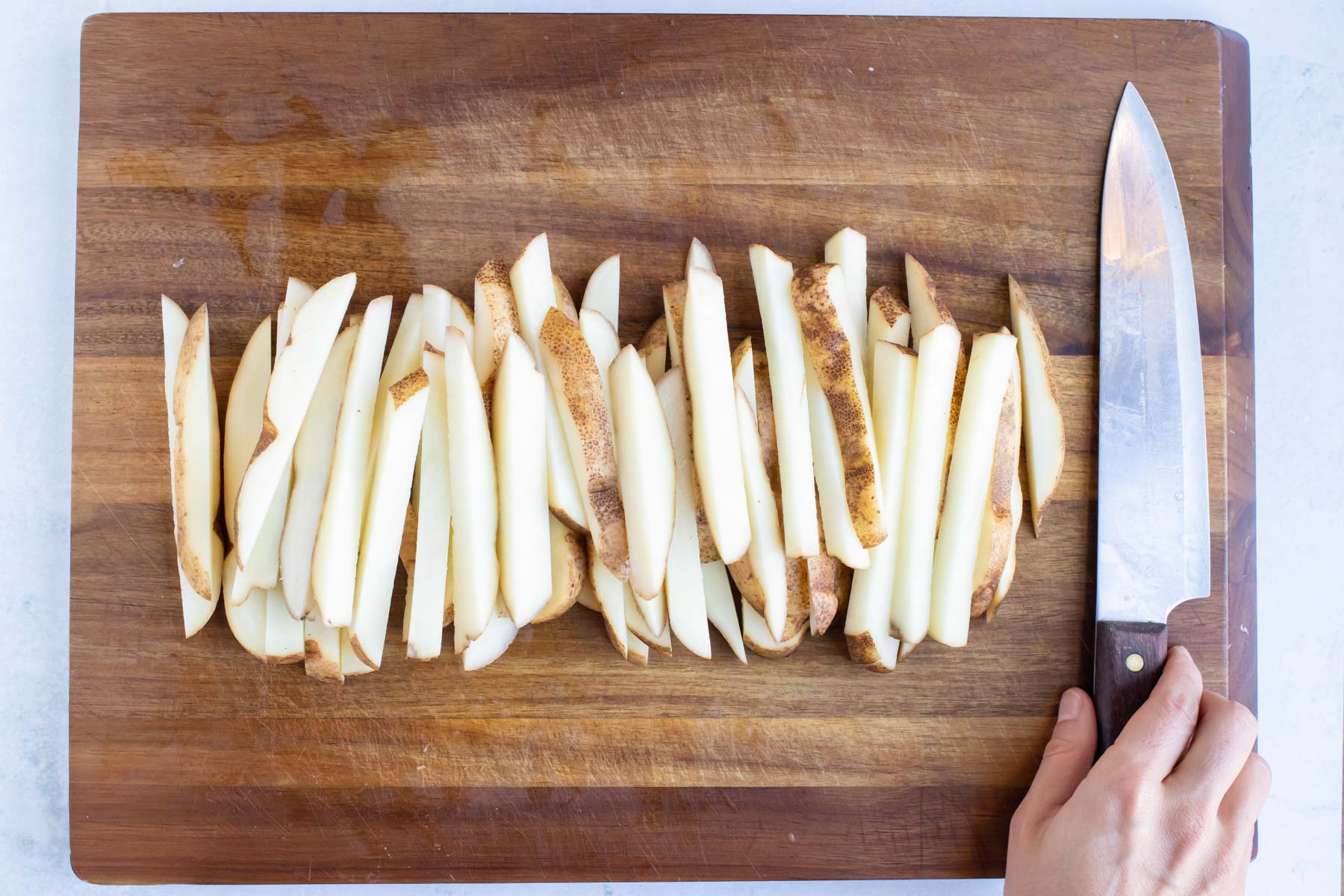 Homemade french fries are prepared on a wooden cutting board.