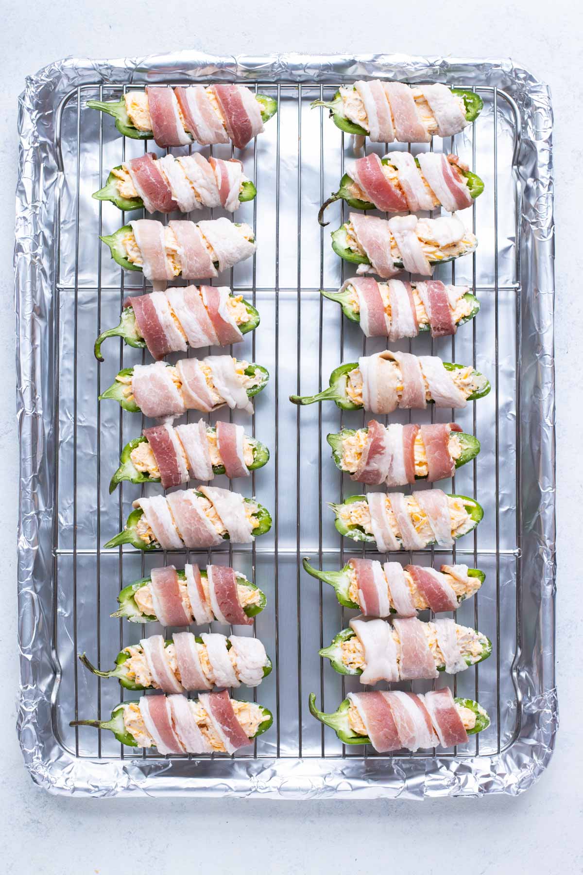 All of the wrapped jalapeno poppers are placed on a baking sheet.
