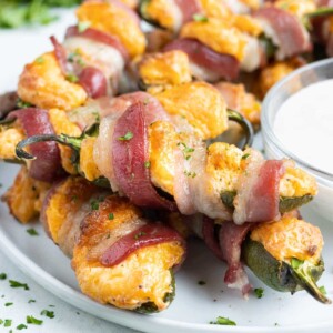 Easy jalapeno poppers wrapped in bacon are served on a white plate.