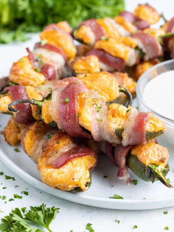Easy jalapeno poppers wrapped in bacon are served on a white plate.