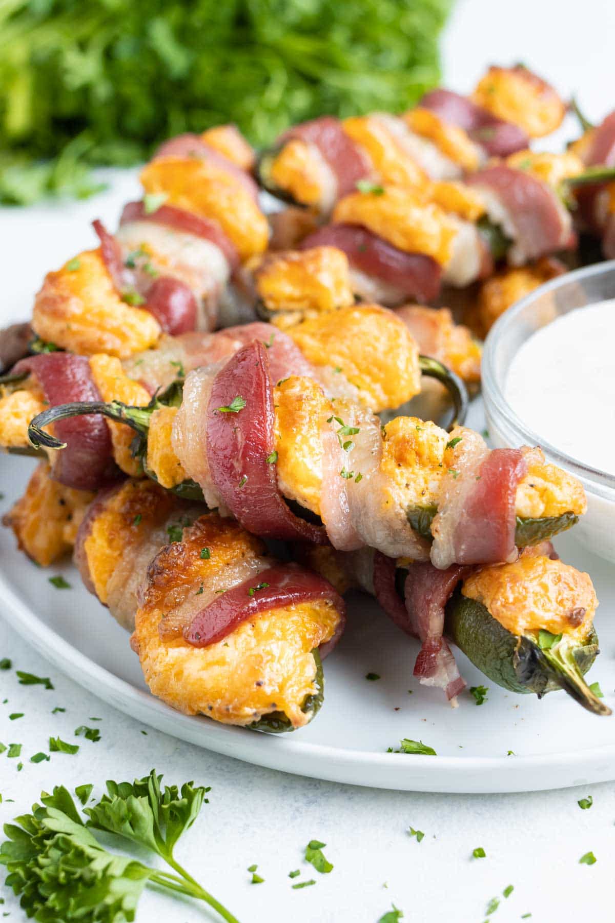 Easy jalapeno poppers wrapped in bacon are served on a white plate.