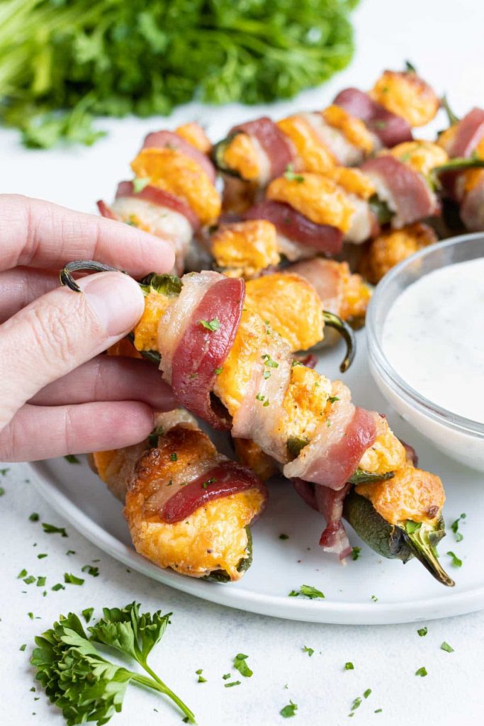 A bacon wrapped jalapeno popper is picked up by a hand for a snack.