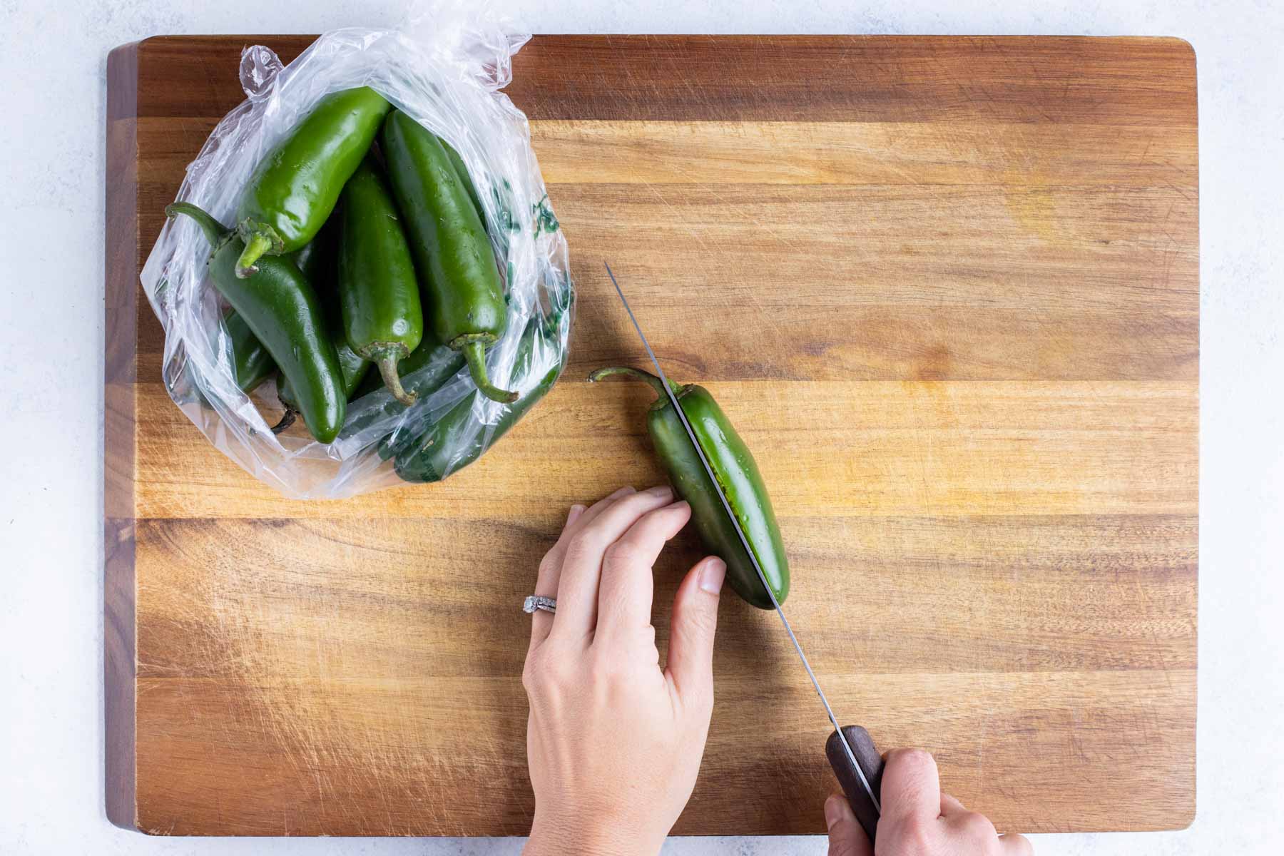 Jalapenos are cut in half with a knife on the counter.