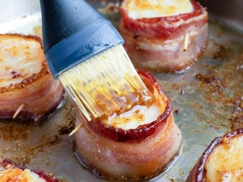 Bacon wrapped scallops being brushed with a garlic butter sauce.