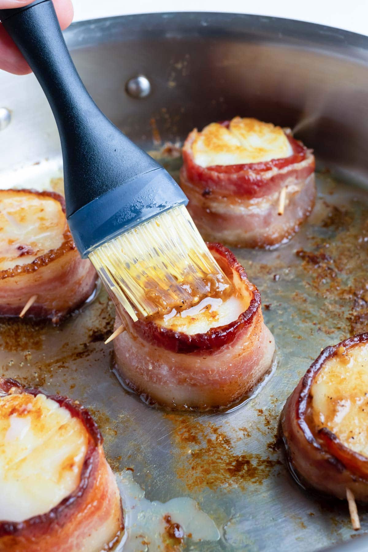 Bacon wrapped scallops being brushed with a garlic butter sauce.