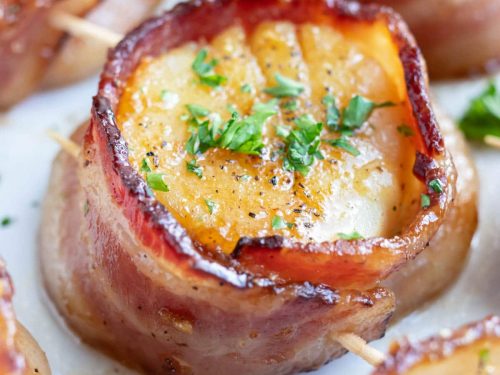A large bacon wrapped scallop with parsley as a garnish.