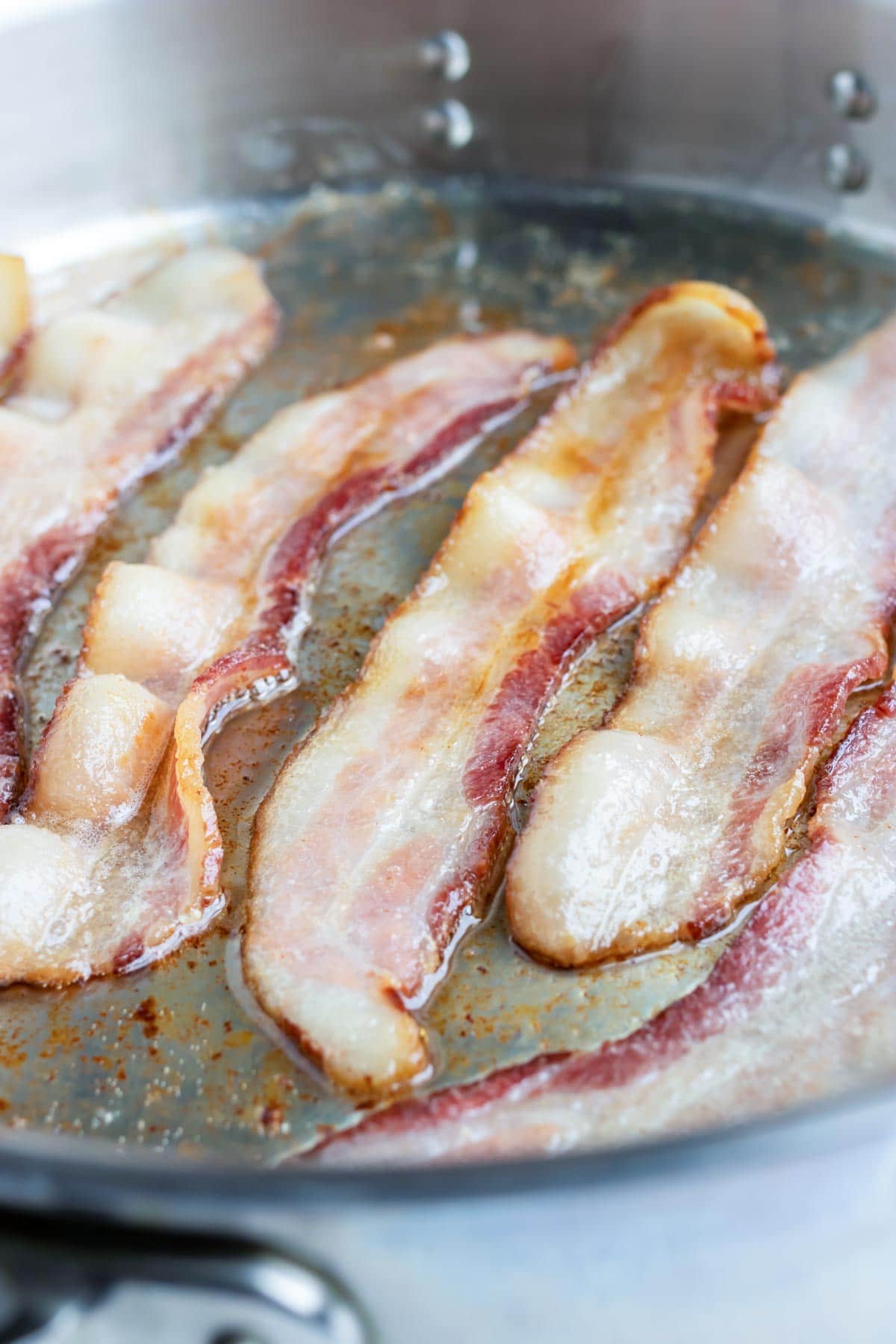 Bacon being cooked in a skillet for a healthy scallop recipe.