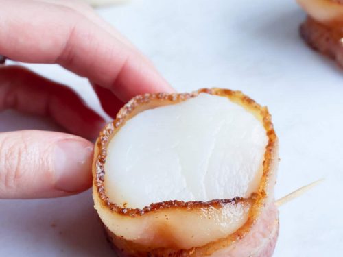A toothpick being inserted into a bacon wrapped scallop