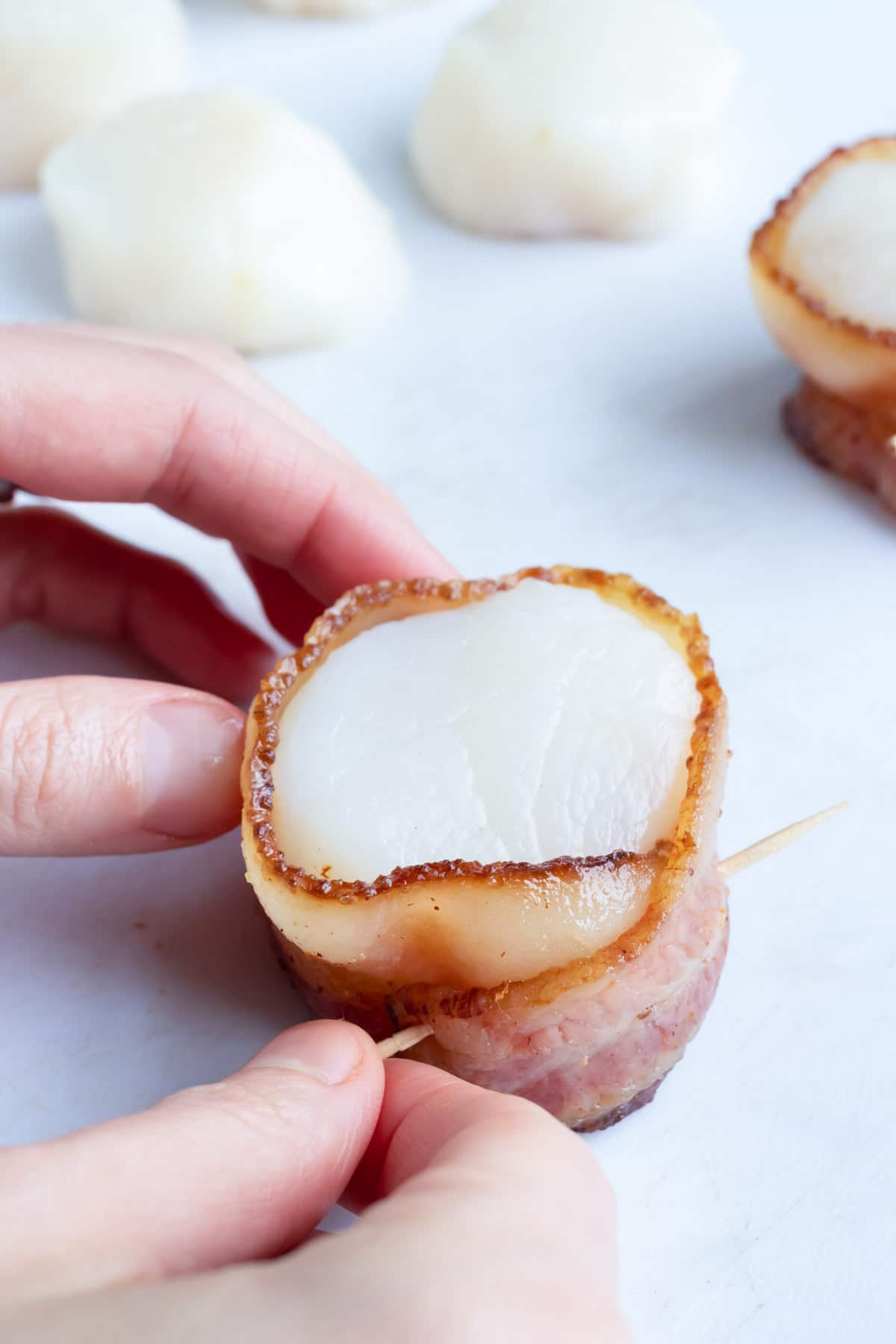 A toothpick being inserted into a bacon wrapped scallop
