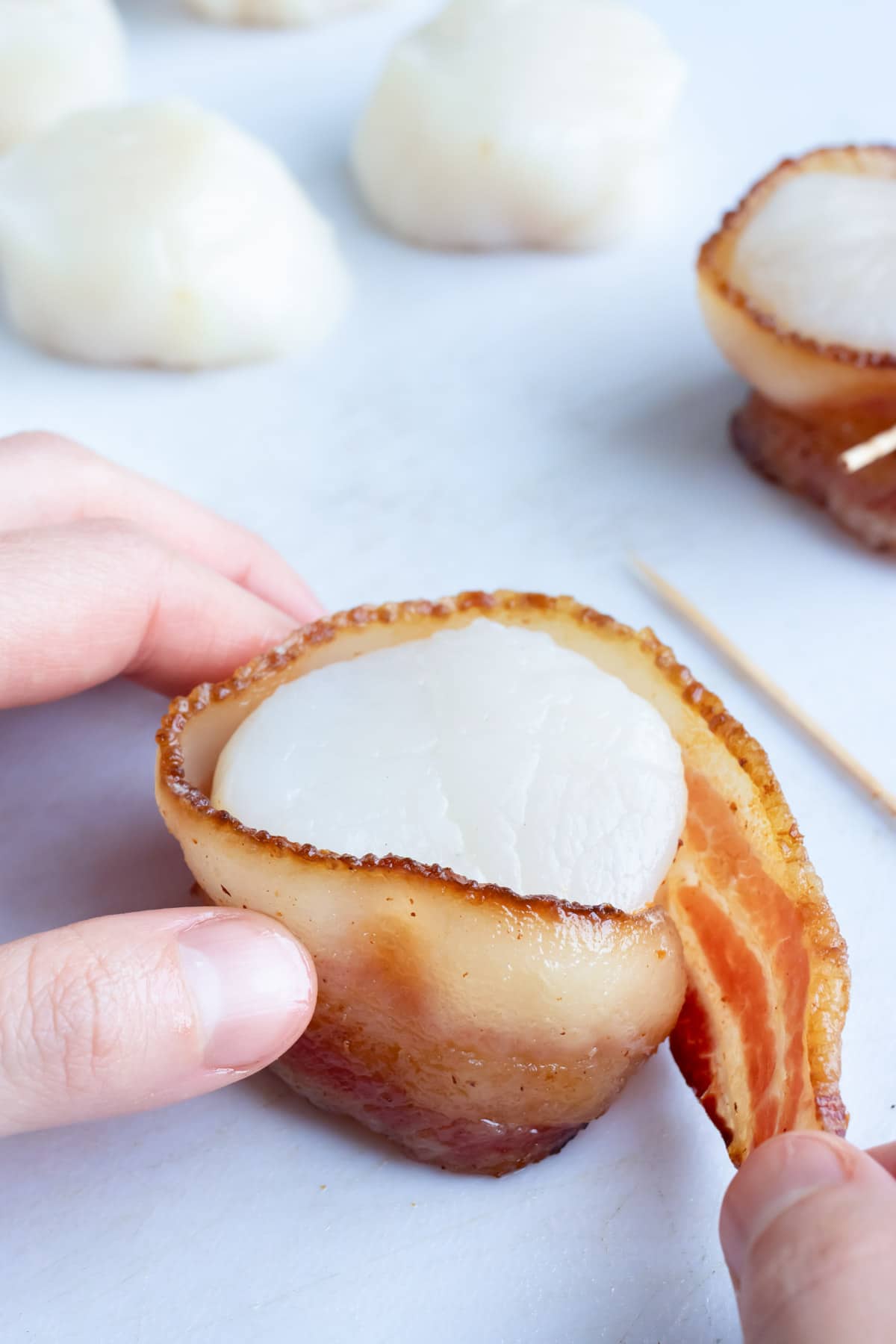 A slice of bacon being wrapped around a scallop.