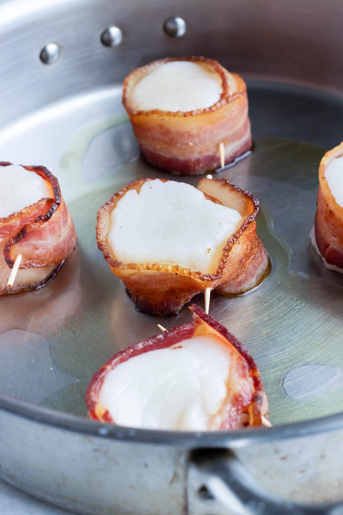 Bacon wrapped scallops being cooked in a skillet.
