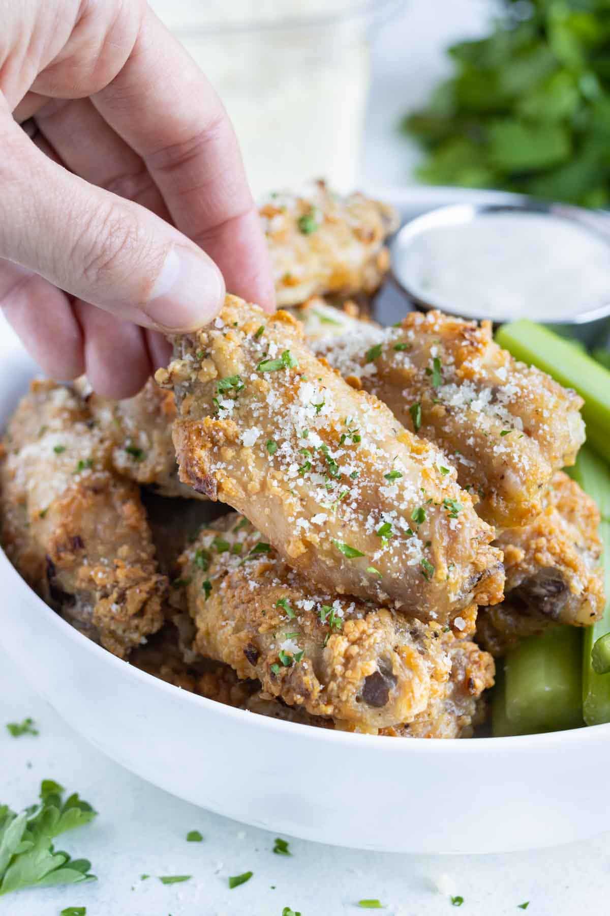 A hand is shown grabbing a chicken wing from the plate.