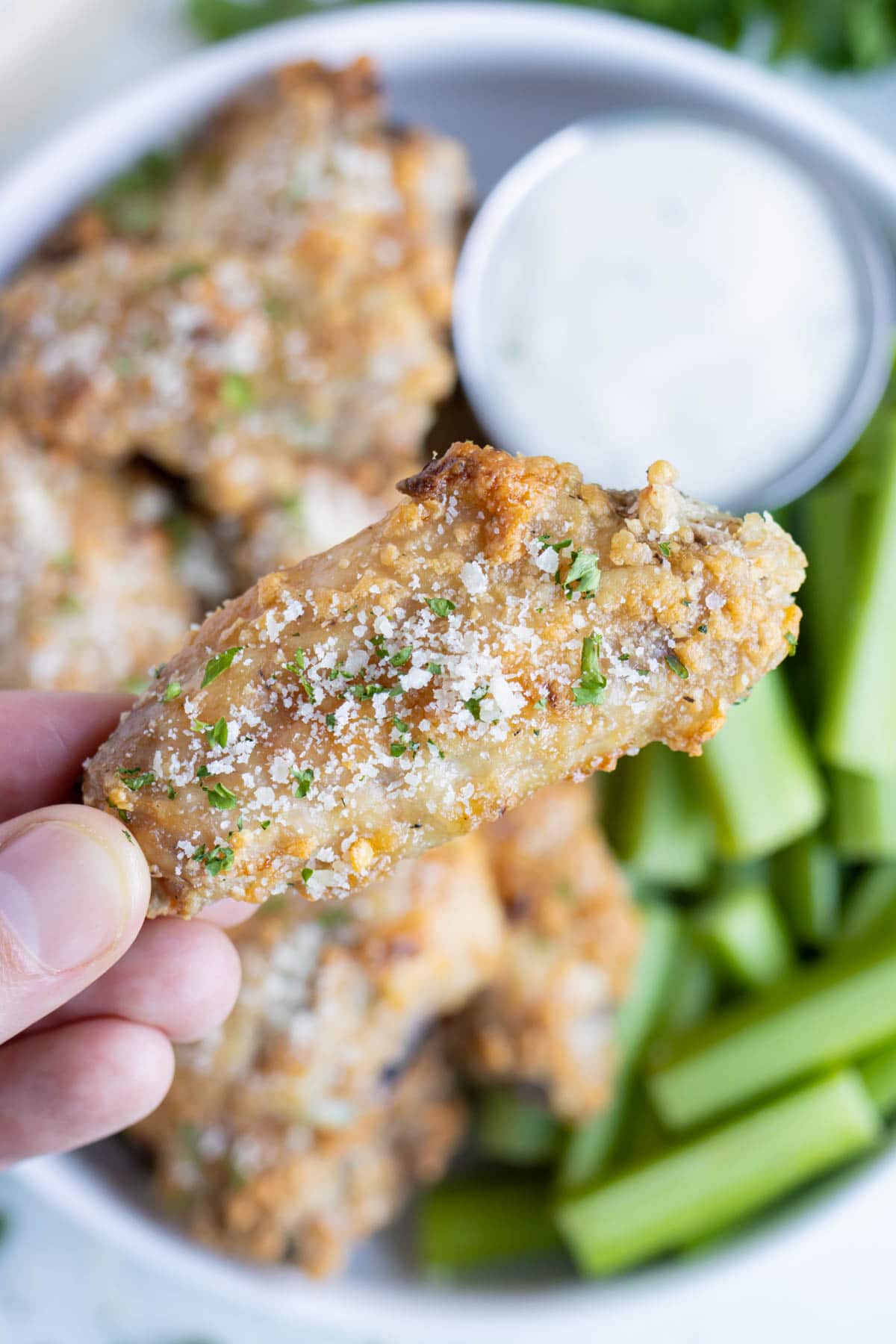 A hand is shown holding the crispy parmesan wing.