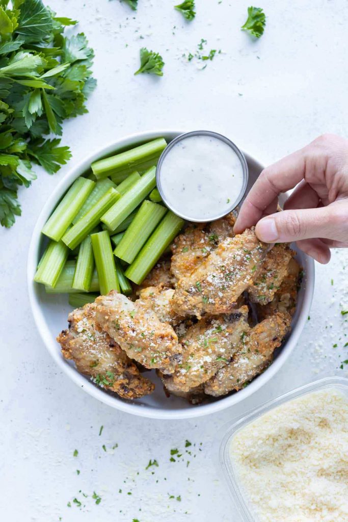 Parmesan garlic chicken wings are picked up by a hand from a plate.