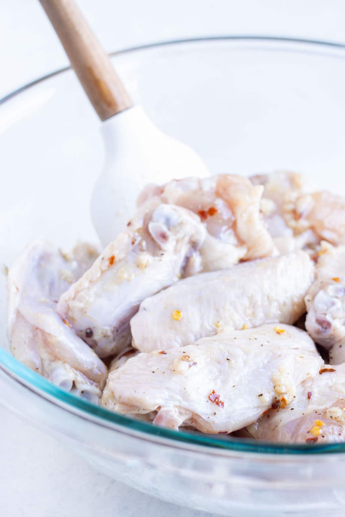 Wings are tossed in the sauce in a bowl.