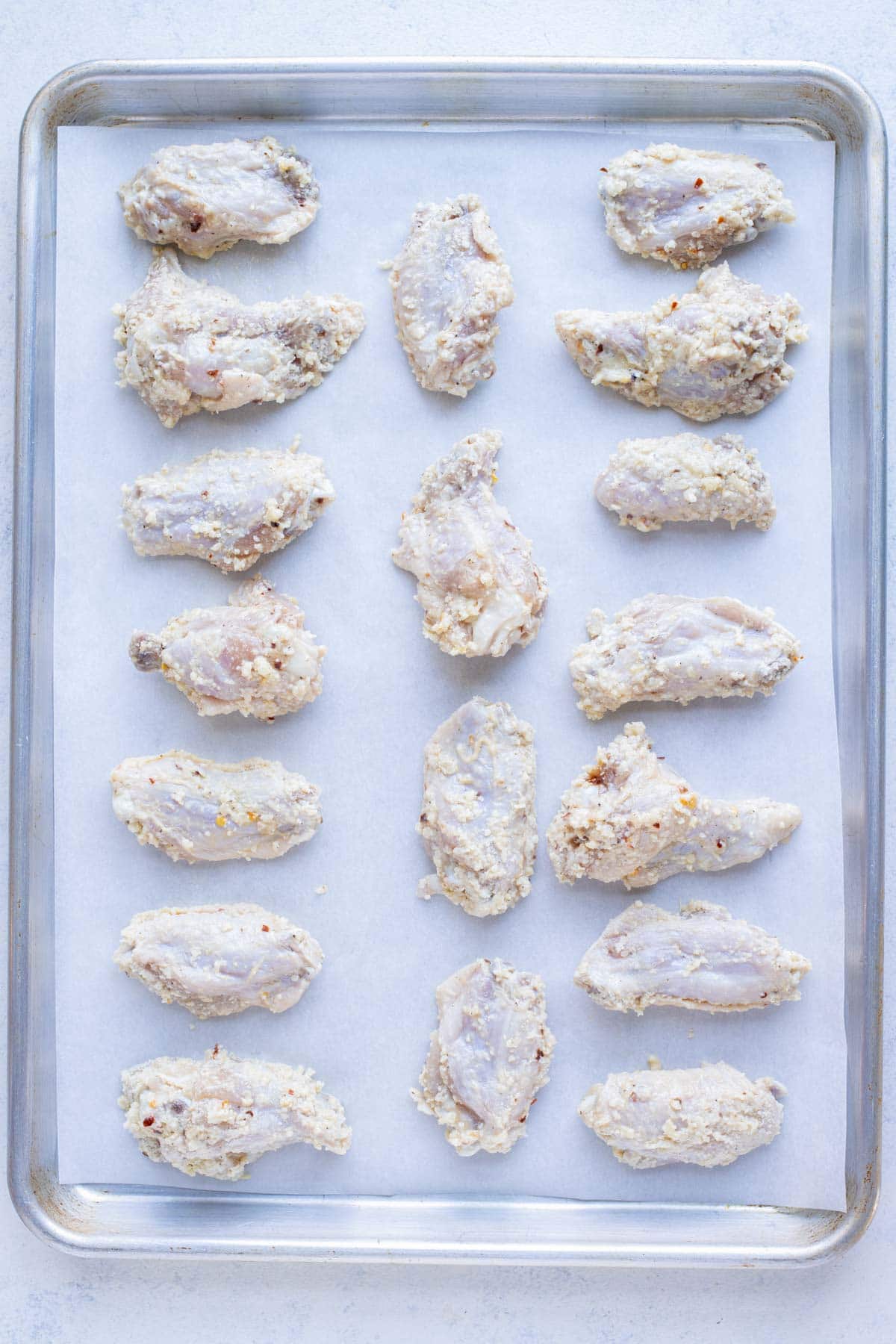 Wings are laid flat on a baking sheet on parchment paper.