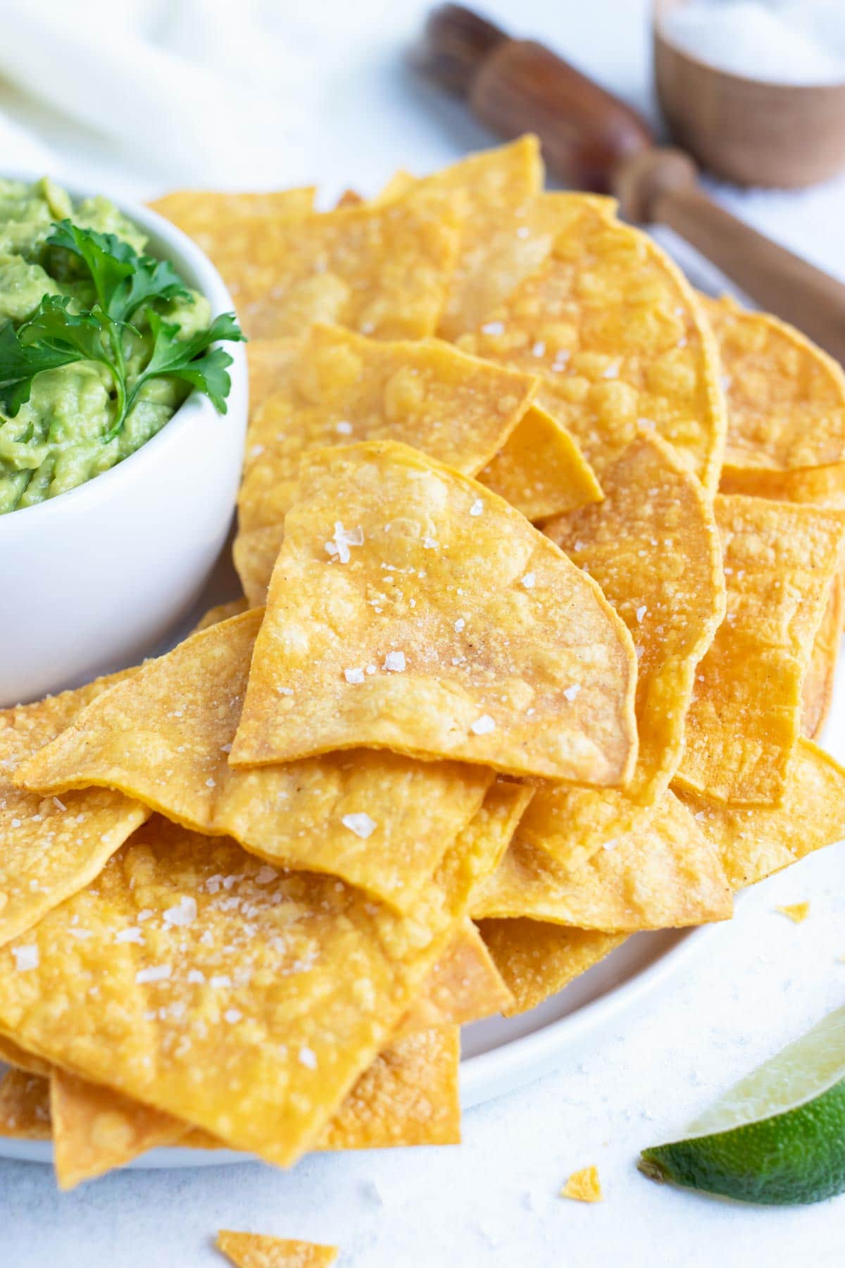 Homemade tortilla chips on a white plate next to a bowl of guacamole.