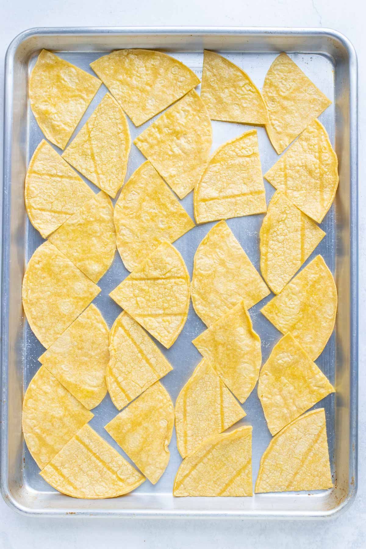 Tortillas cut into triangles arranged on a baking sheet. 