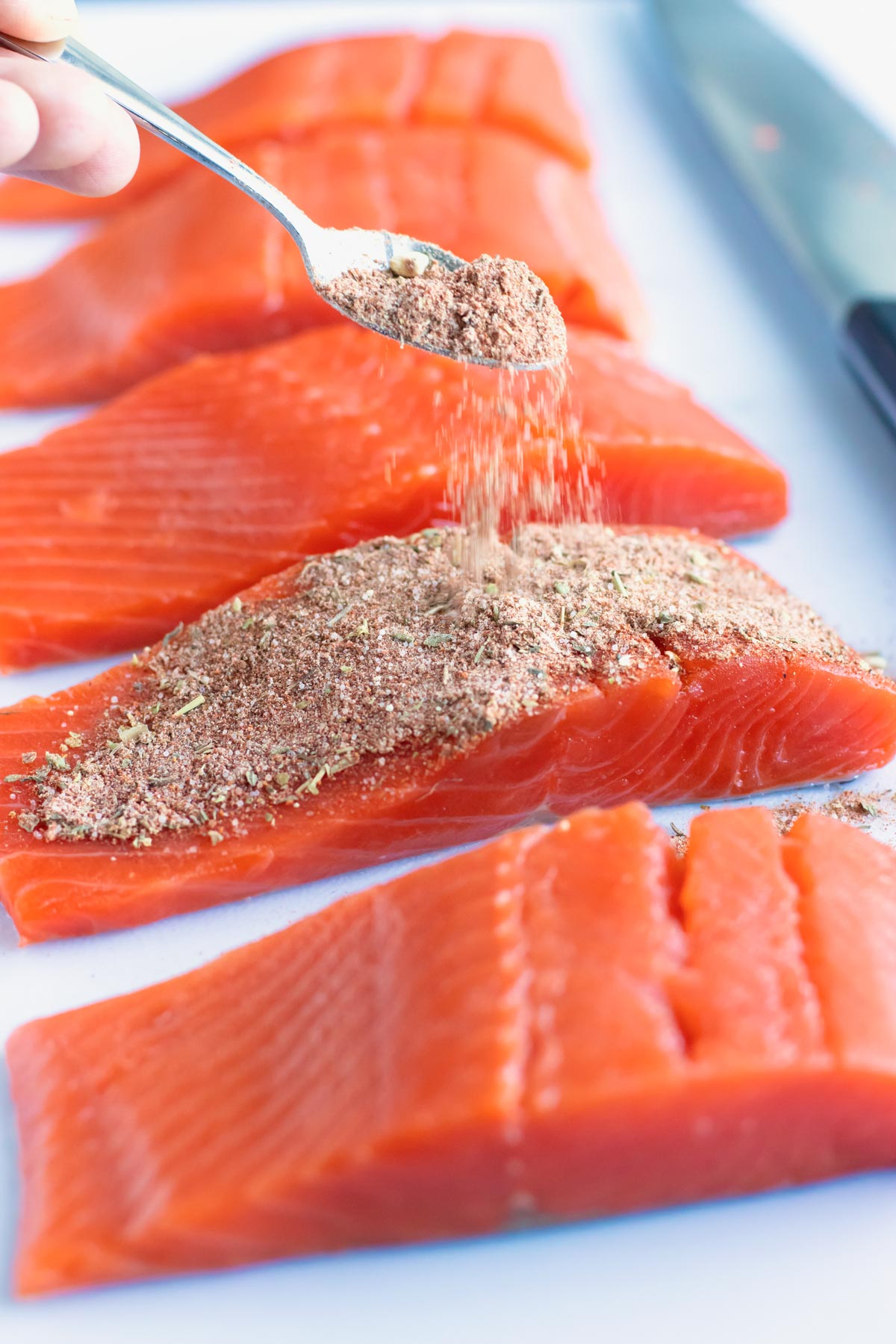 Homemade seasoning mix being sprinkled over salmon to make a blackened salmon recipe.