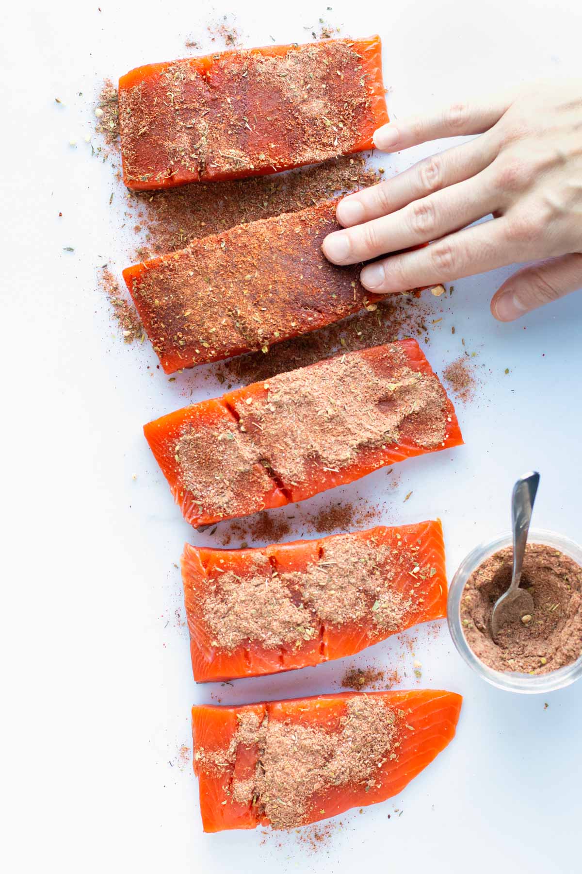 Blackened seasoning mix being rubbed into salmon filets on a white cutting board.