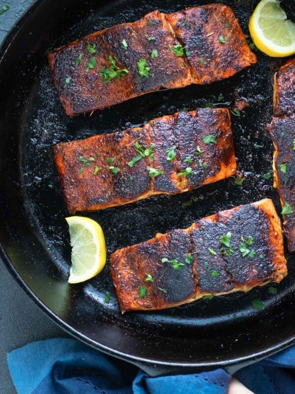 Cajun blackened salmon fillets in a cast-iron skillet with lemon wedges.