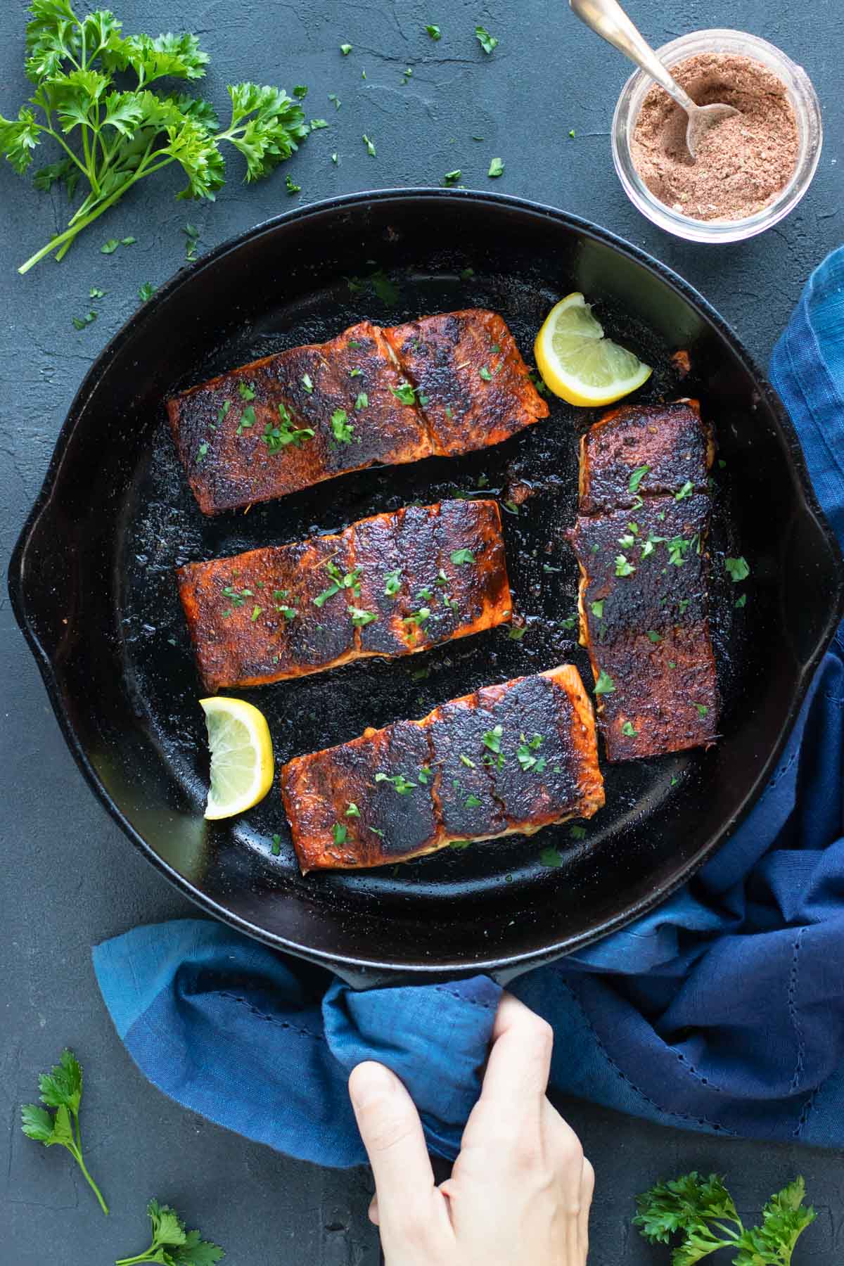 Blackened salmon recipe in a black cast iron skillet with a bowl full of blackened seasoning next to it.