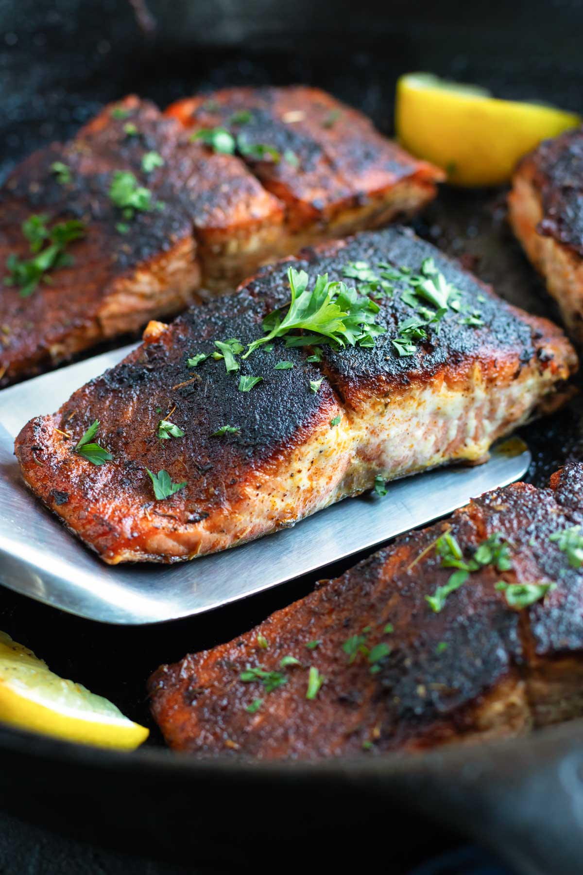 Blackened salmon in a cast iron skillet with lemons and parsley.