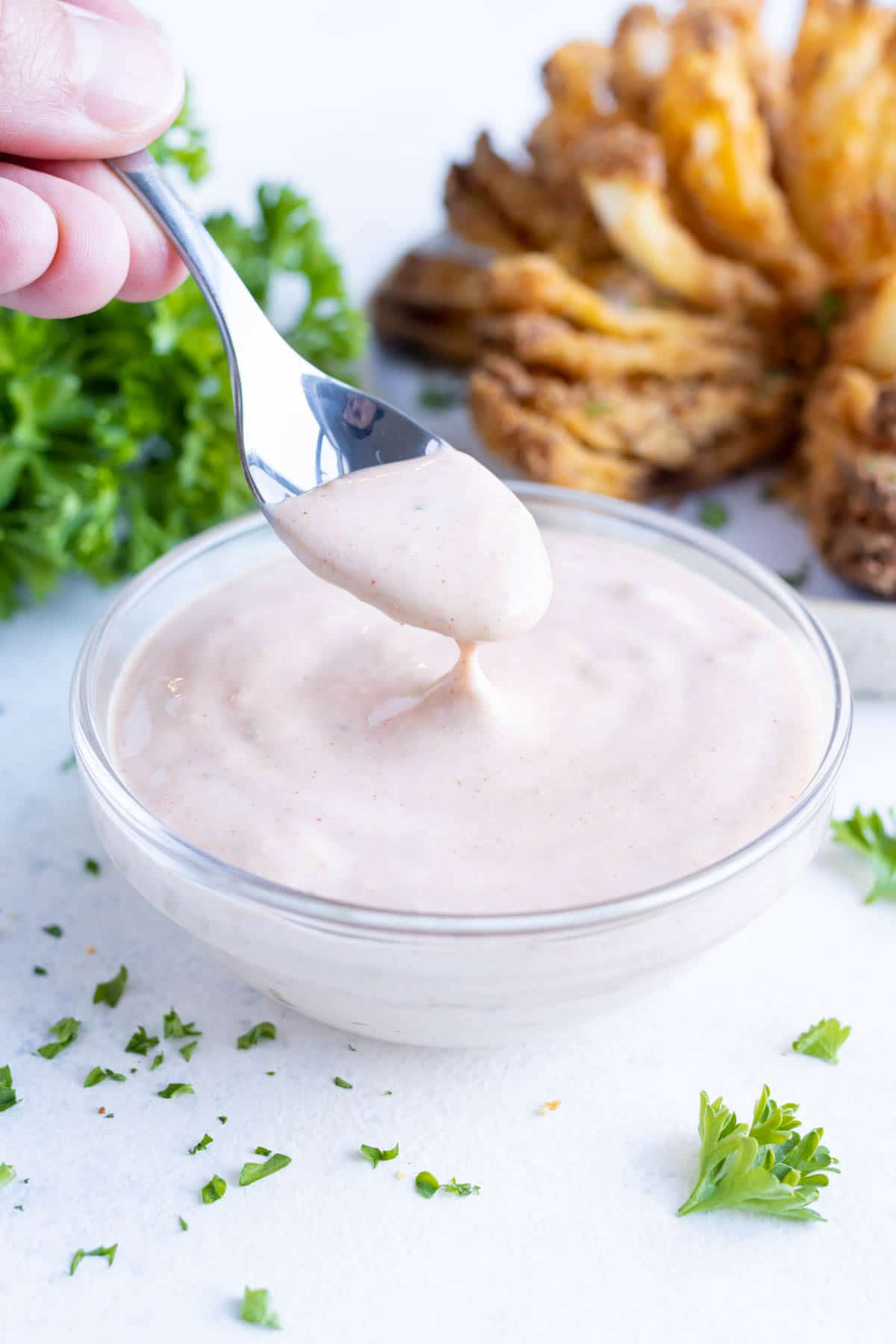 A metal spoon is used to serve the blooming onion sauce from a bowl.