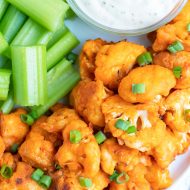 A white plate full of buffalo cauliflower bites, celery sticks, and a bowl full of ranch dressing for a Super Bowl appetizer.