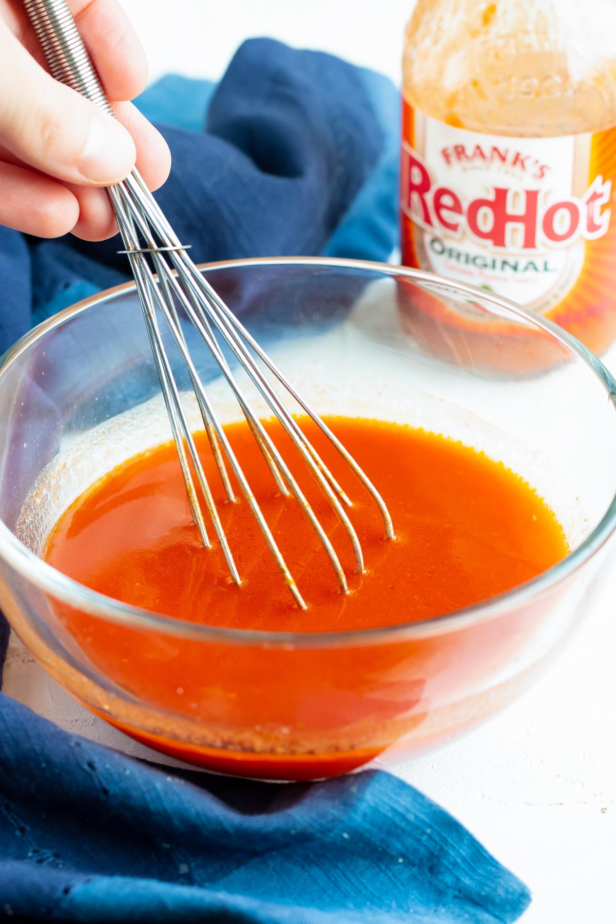 Buffalo sauce being whisked together in a clear bowl with Frank's red hot sauce in the background.