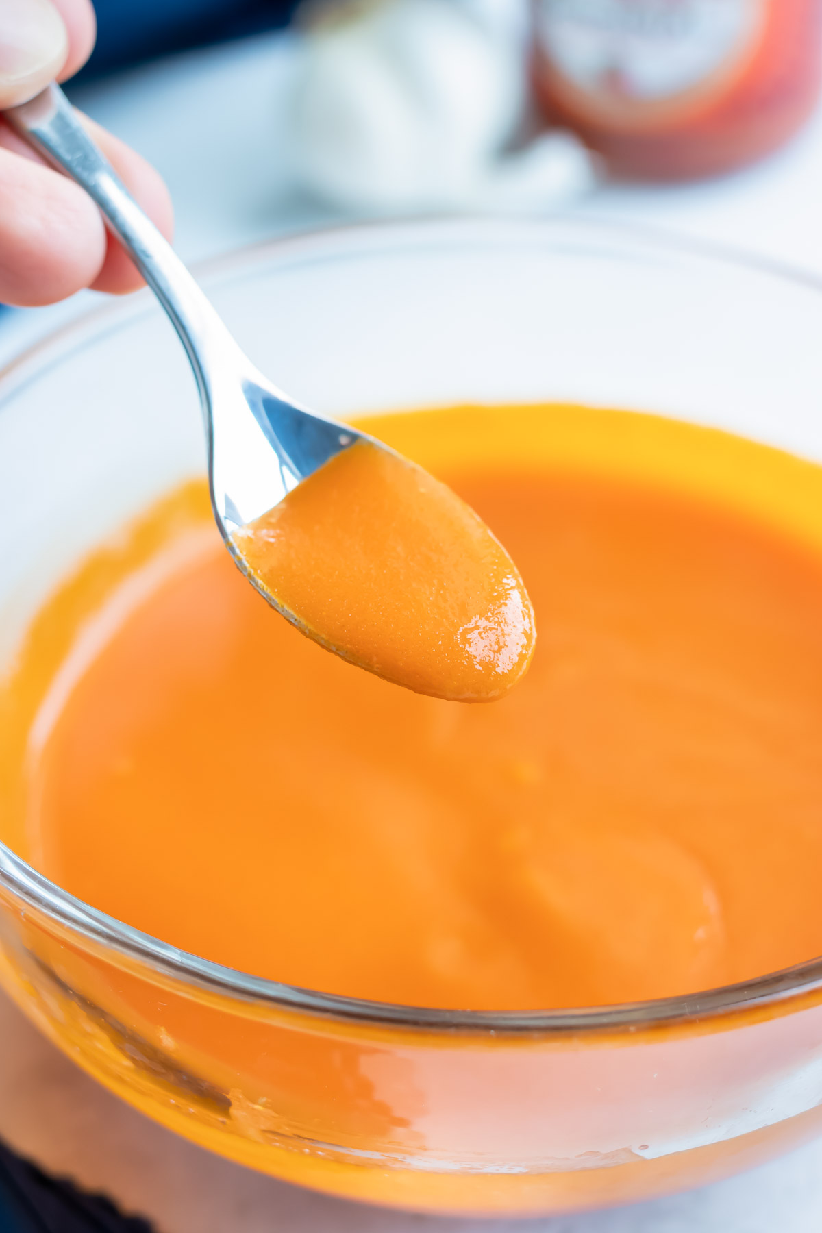 Thick buffalo wing sauce coating the back of a spoon over a glass bowl.