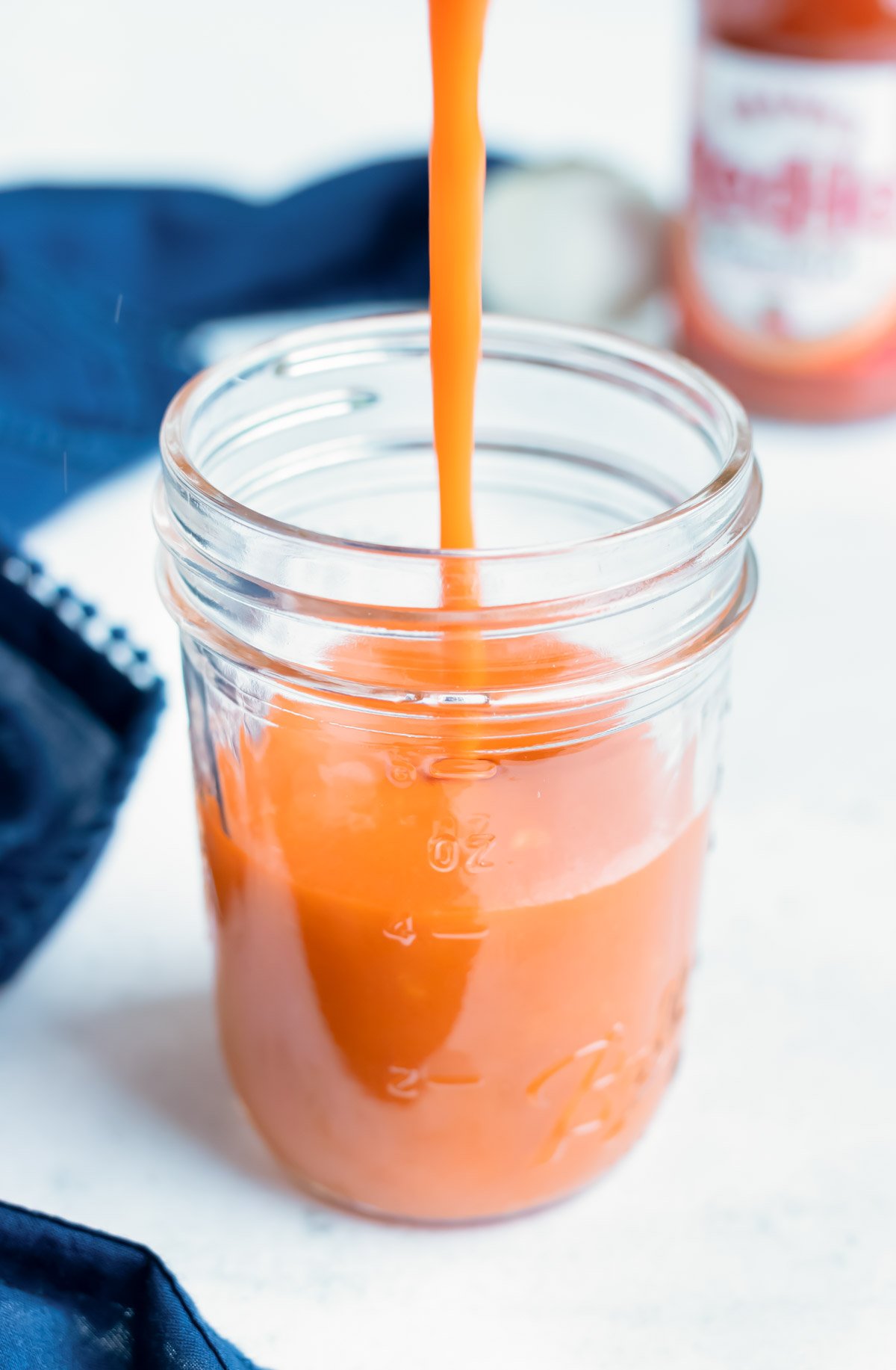 Buffalo wing sauce is poured into a mason jar.