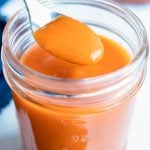 Spicy buffalo wing sauce is lifted up with a spoon before putting on wings.