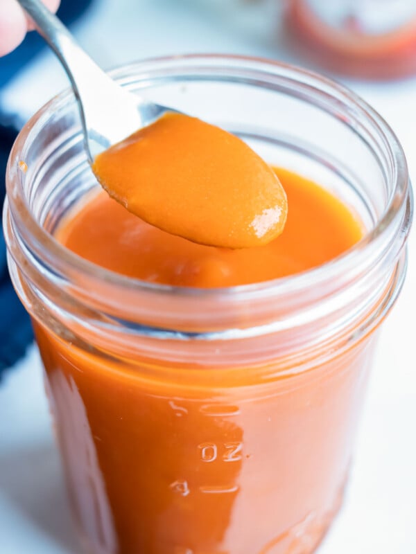 Spicy buffalo wing sauce is lifted up with a spoon before putting on wings.
