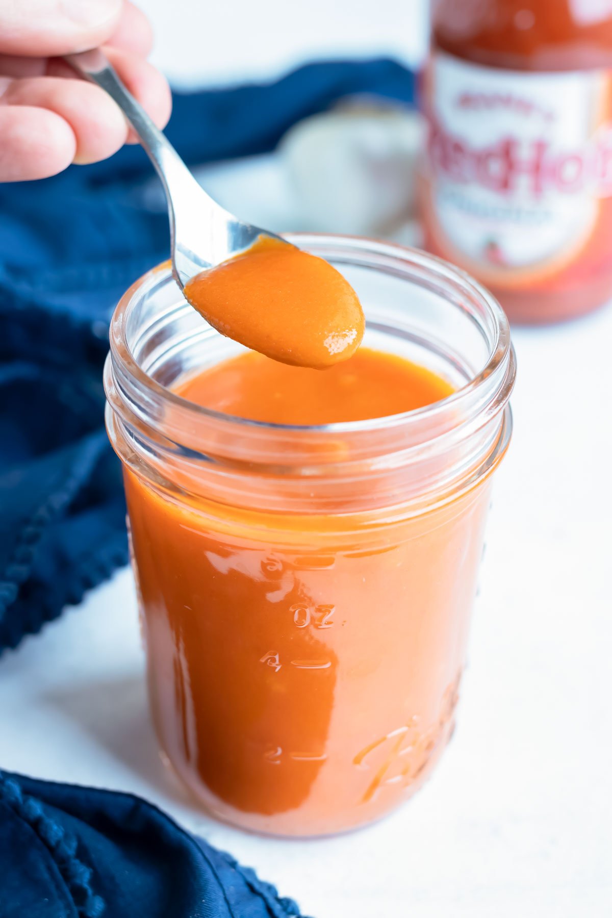 Buffalo sauce is lifted out of a mason jar with a spoon.