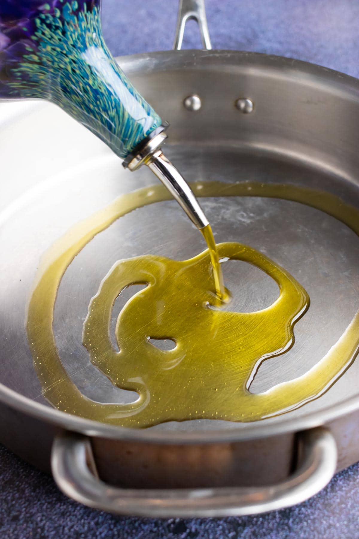 An image showing oil being added to a stainless steel pan.