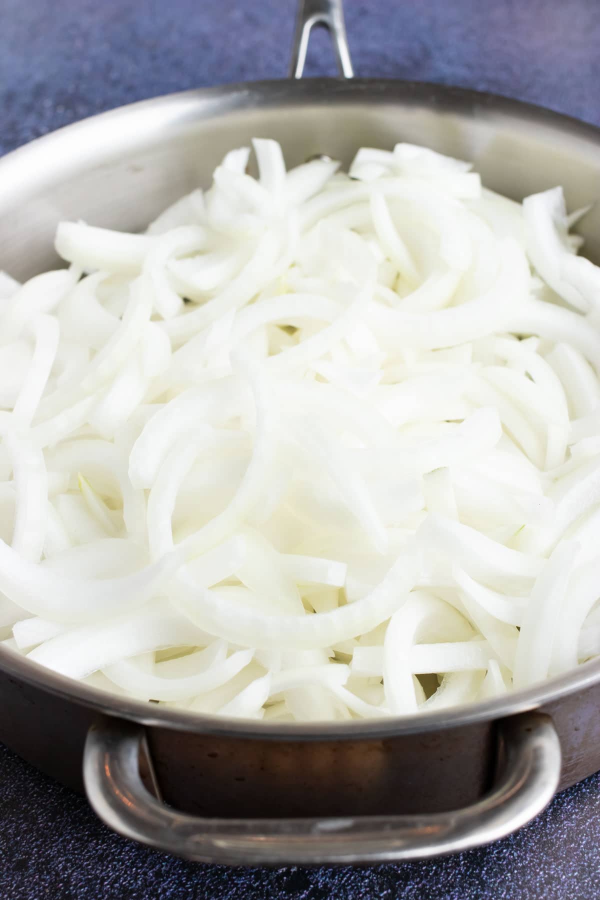 An image showing sliced onions being added to a stainless steel pan.