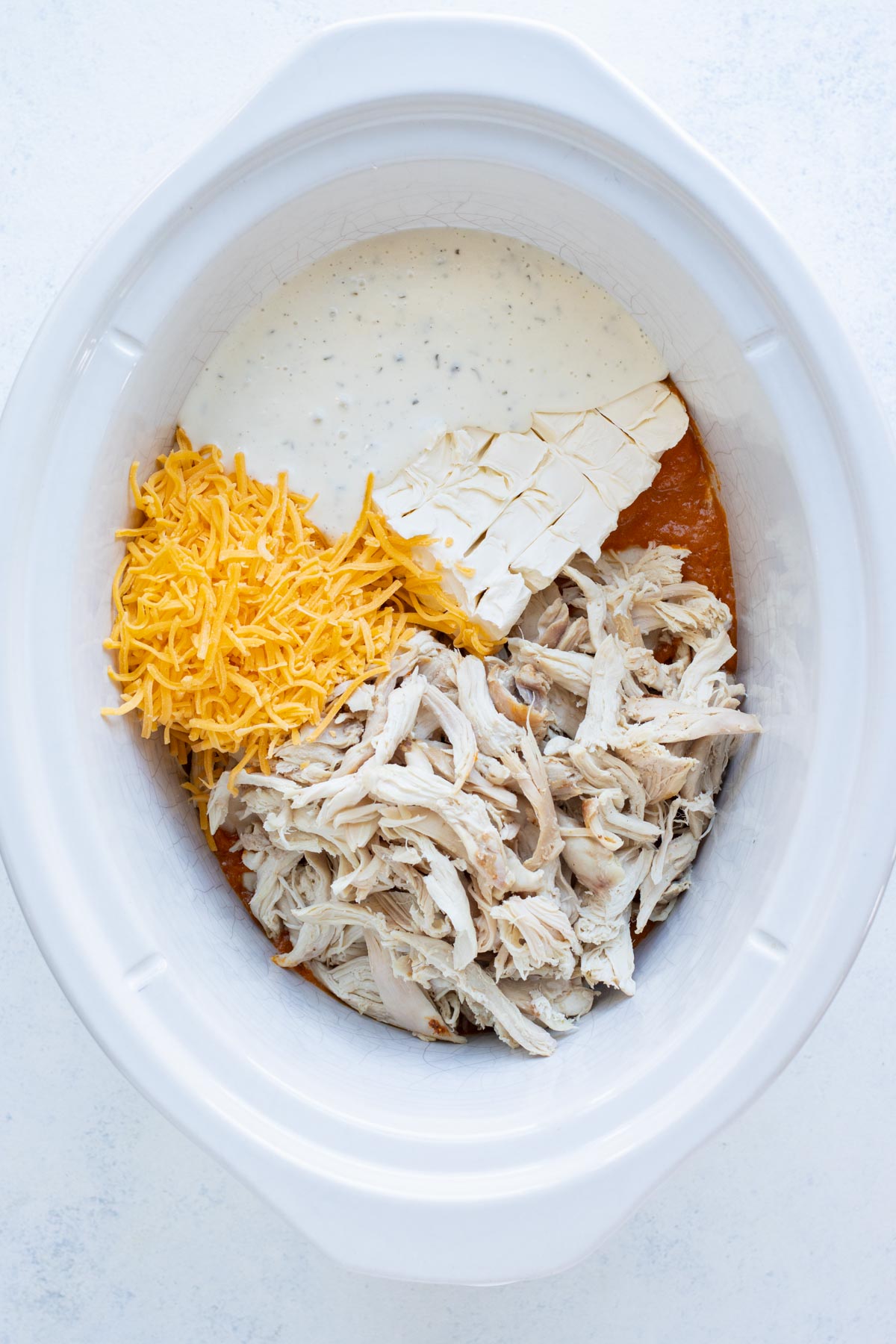 Cream cheese, cheddar cheese, ranch, and shredded chicken are added to the crockpot.