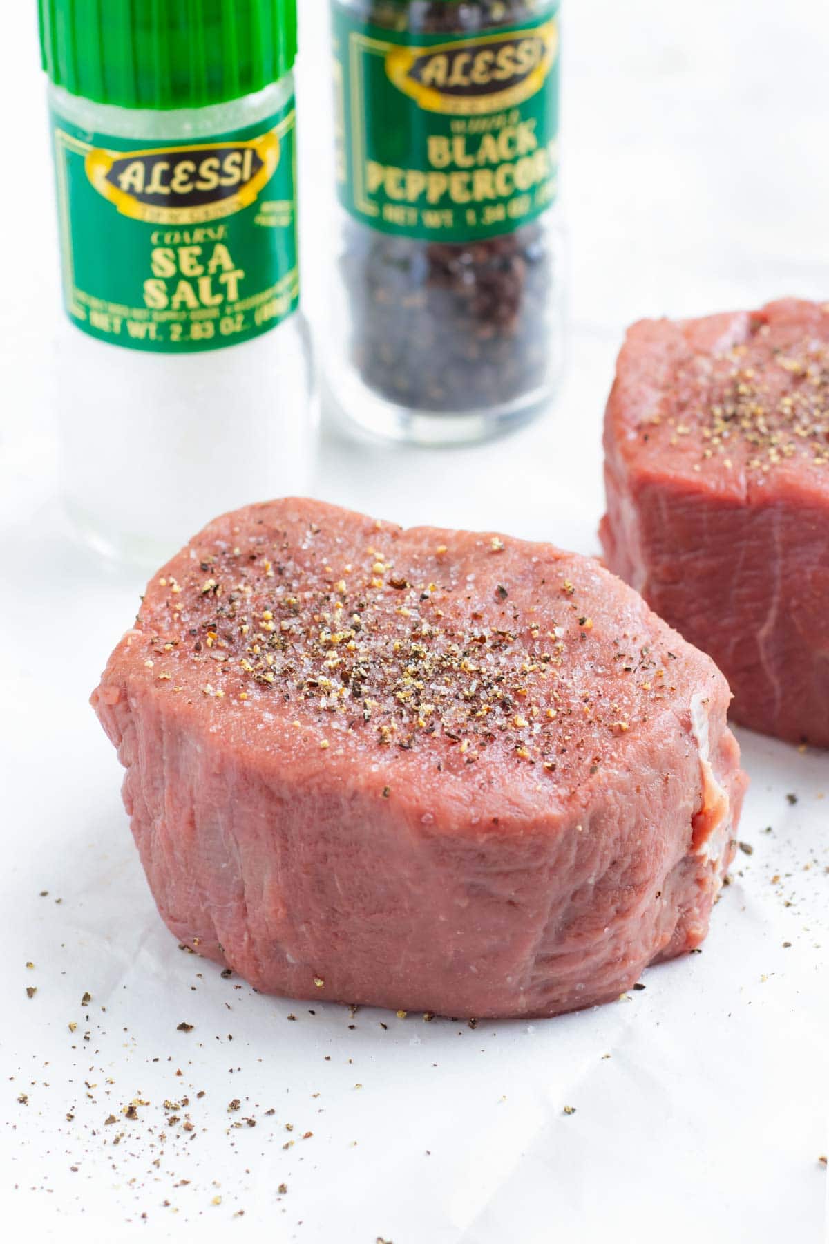 A two-inch thick grass-fed filet mignon steak with a salt and pepper shaker in the back ground.