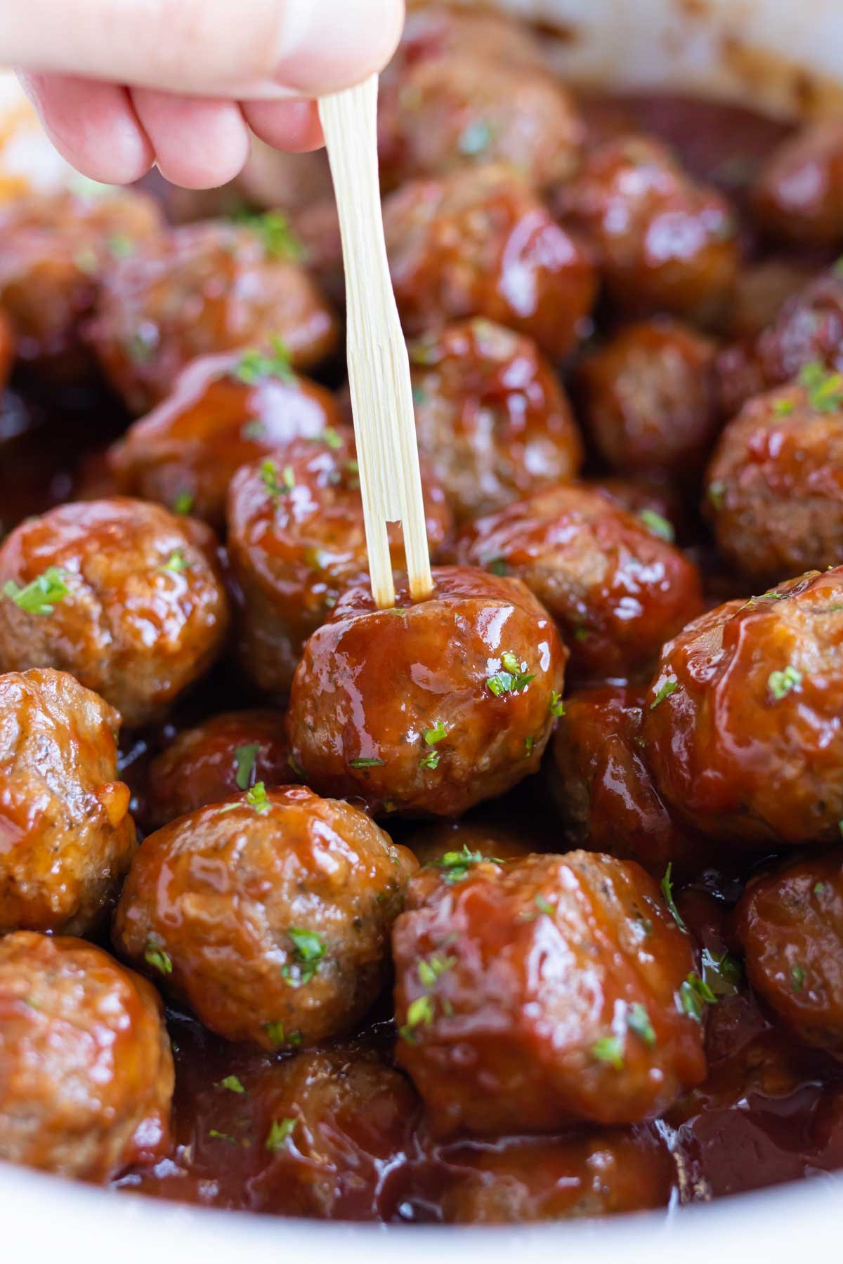 A toothpick is shown picking up a grape jelly meatball.