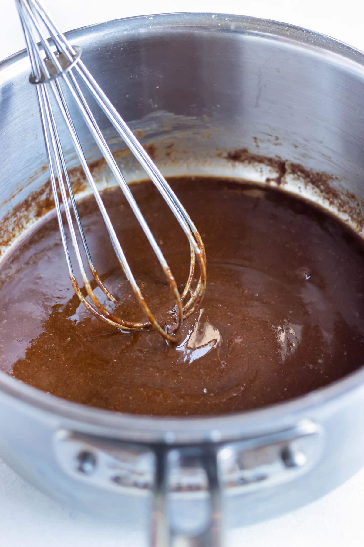 A whisk is used to stir a dark brown roux.
