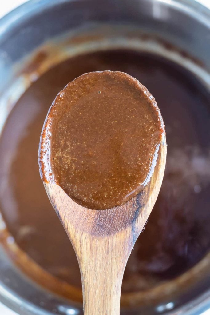 A dark roux for gumbo is lifted out of the pot with a wooden spoon.