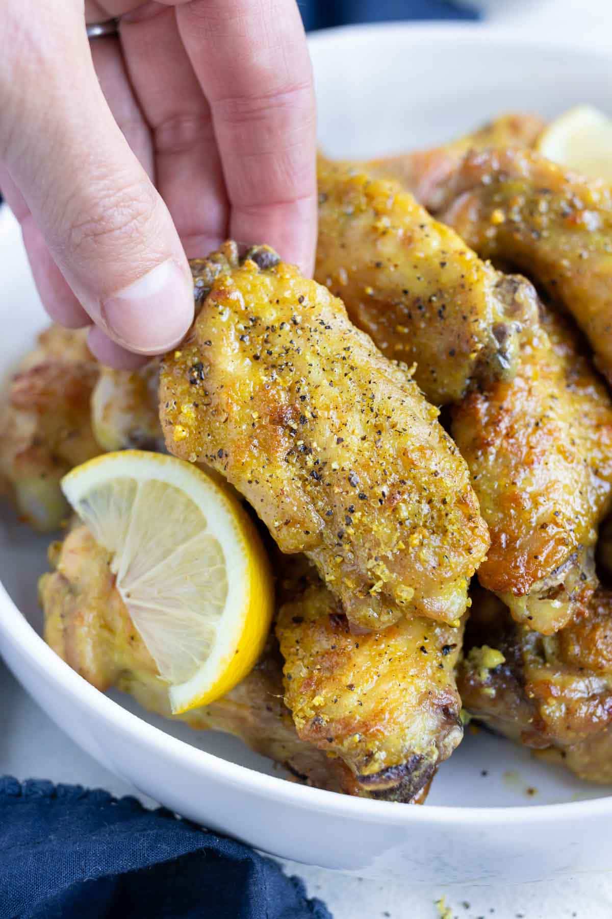 A hand is shown picking up a crispy lemon pepper chicken wing.