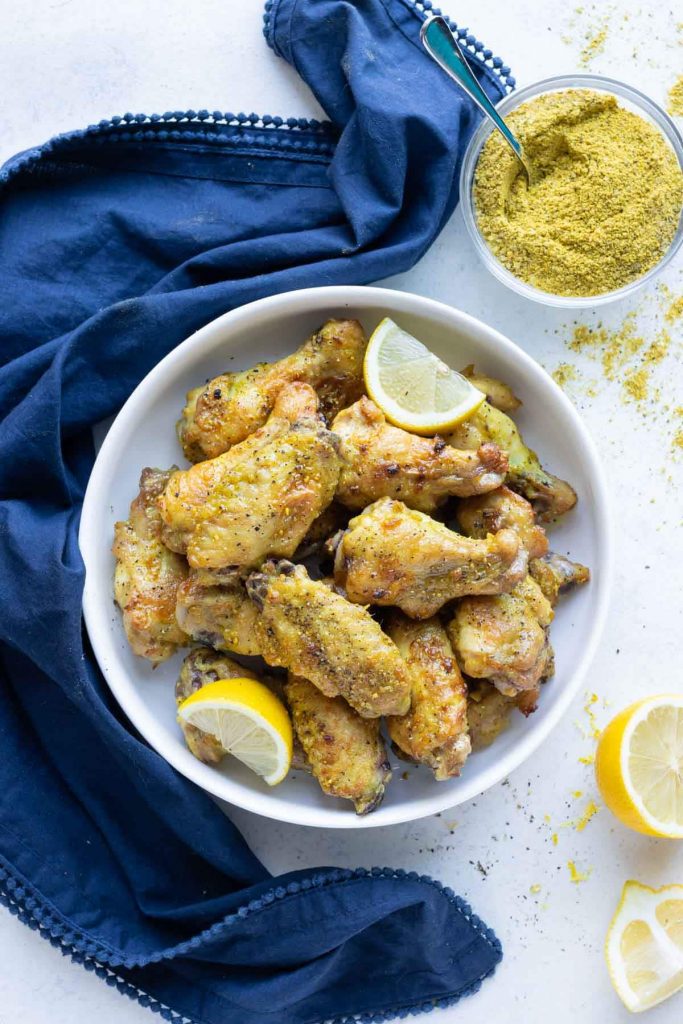 A bowl of chicken wings is shown on the counter with fresh lemons.