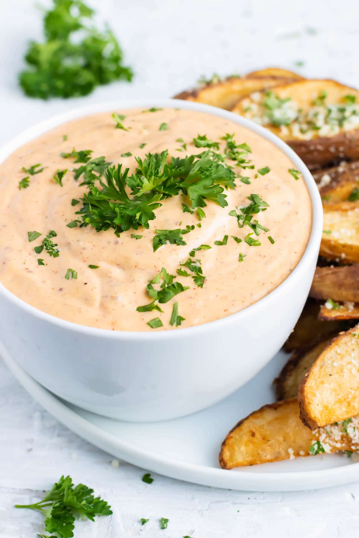 A bowl full of remoulade sauce next to a plate of baked potato wedges.