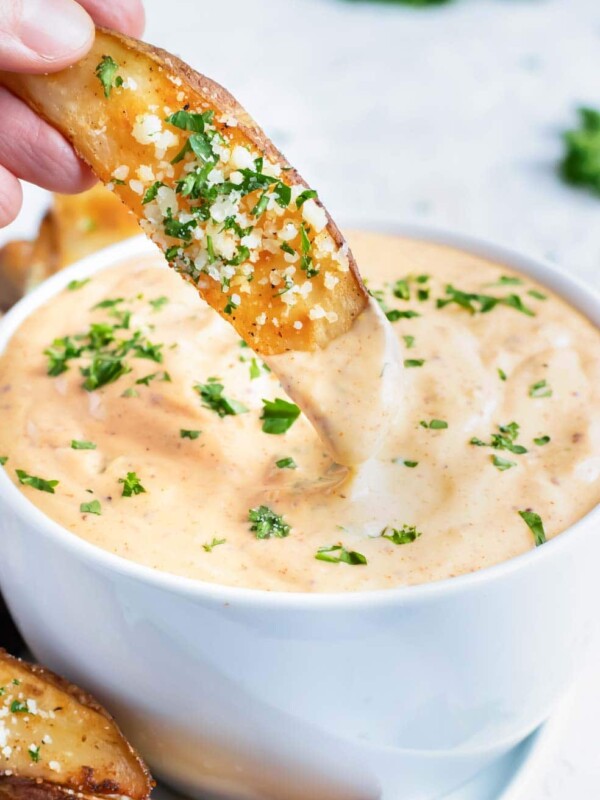 A baked potato wedge being dipped into a bowl full of Cajun remoulade sauce.